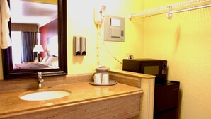 A hotel bathroom with a sink, mirror, towel dispenser, and a small refrigerator. - Polynesian Inn (St. Cloud)