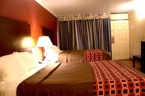 A hotel room with two beds, a lamp, a curtain, and a door.