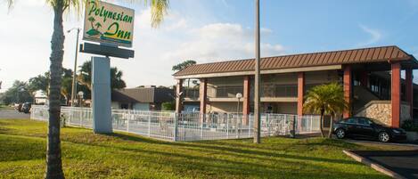 A sign for the Polynesian Inn, a building with a covered parking area, and a street lamp.