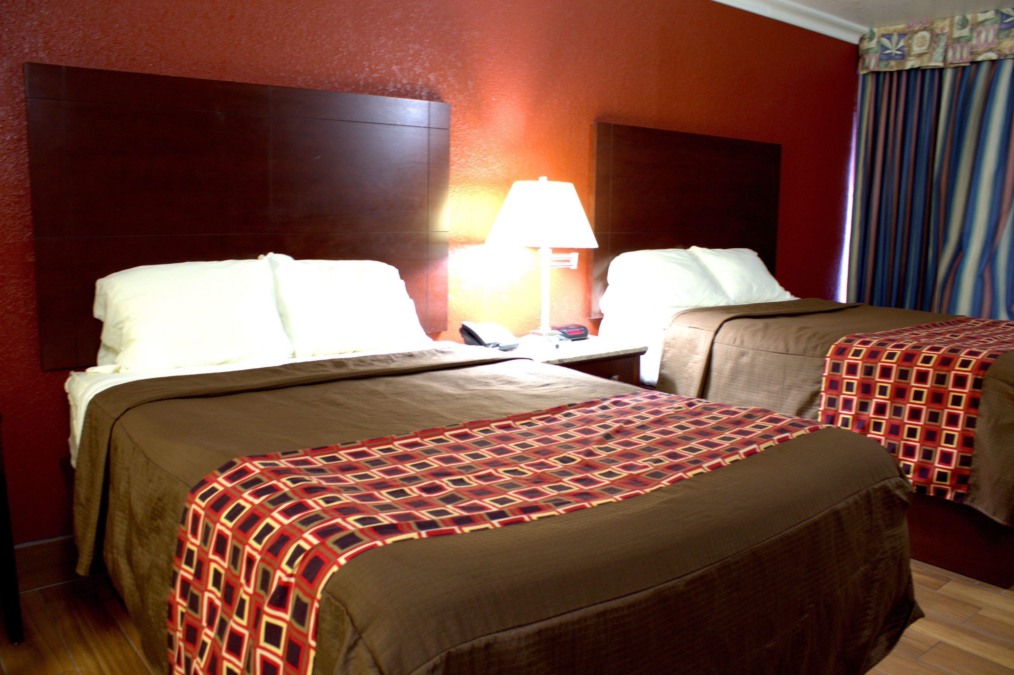 A hotel room with two beds, a nightstand, a lamp, and a window with curtains.