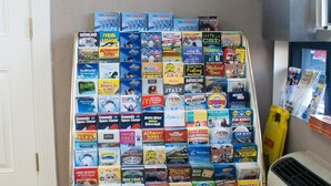 A display rack filled with various magazines and books in a room with a tiled floor and a window. - Polynesian Inn (St. Cloud)