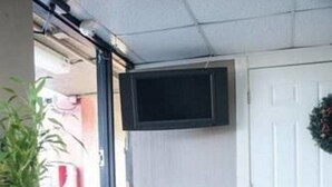 A room with a tiled floor, a potted plant, a small table, a wall-mounted TV, and a door. - Polynesian Inn (St. Cloud)