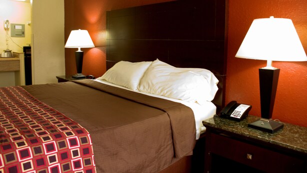 A hotel room with a large bed, two bedside lamps, a telephone, and a nightstand. - Polynesian Inn (St. Cloud)