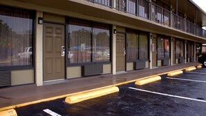 A building with multiple doors and windows, a parking lot with marked spaces, and a balcony on the upper floor. - Polynesian Inn (St. Cloud)