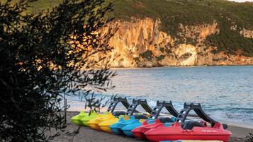 Una fila de motos acuáticas coloridas alineadas en una playa arenosa, con un acantilado y el océano al fondo.