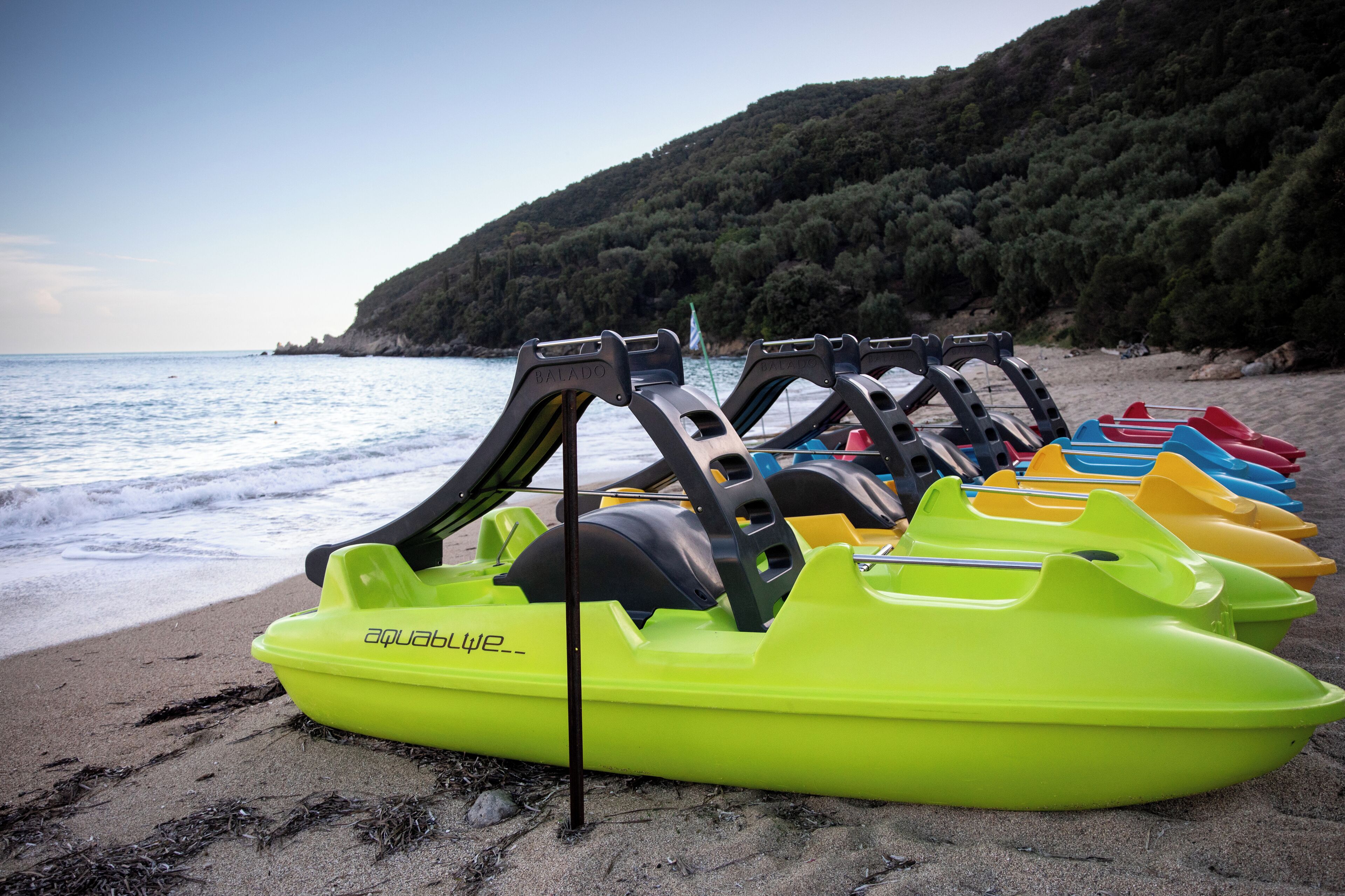 Une rangée de bateaux gonflables aux couleurs vives sur une plage, avec une colline boisée en arrière-plan.