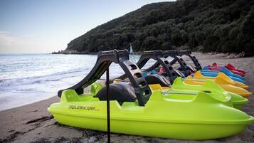 Une rangée de bateaux gonflables aux couleurs vives sur une plage, avec une colline boisée en arrière-plan.