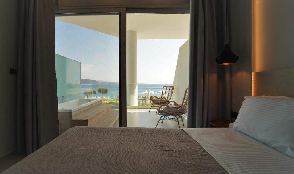 Un dormitorio con una cama grande, vista al mar y un balcón con sillas.