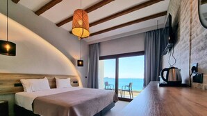 A modern hotel room with a curved ceiling, a large bed, a wooden table, and a view of the sea through the window. - Enjoy Lichnos Bay Village, Camping, Hotel & Apartments (Parga)