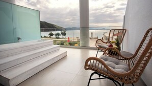 A balcony with wicker chairs, a glass railing, and a view of the sea. - Enjoy Lichnos Bay Village, Camping, Hotel & Apartments (Parga)