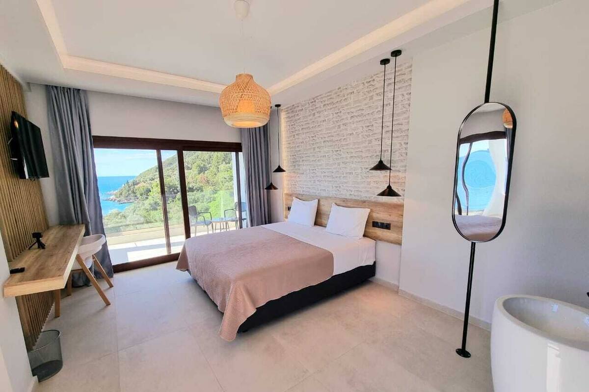 A modern hotel room with a large bed, a desk, and a view of the sea.