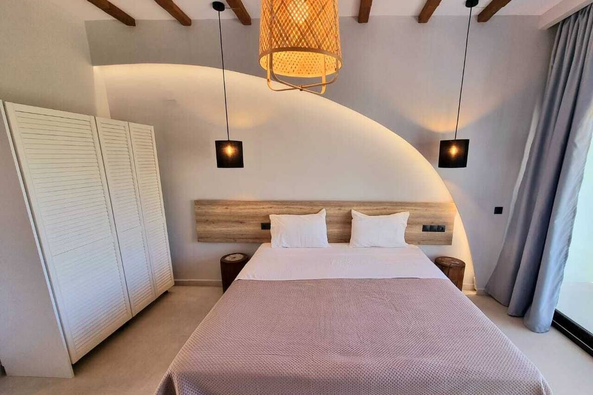 A modern bedroom with a large bed, wooden headboard, and pendant lights.