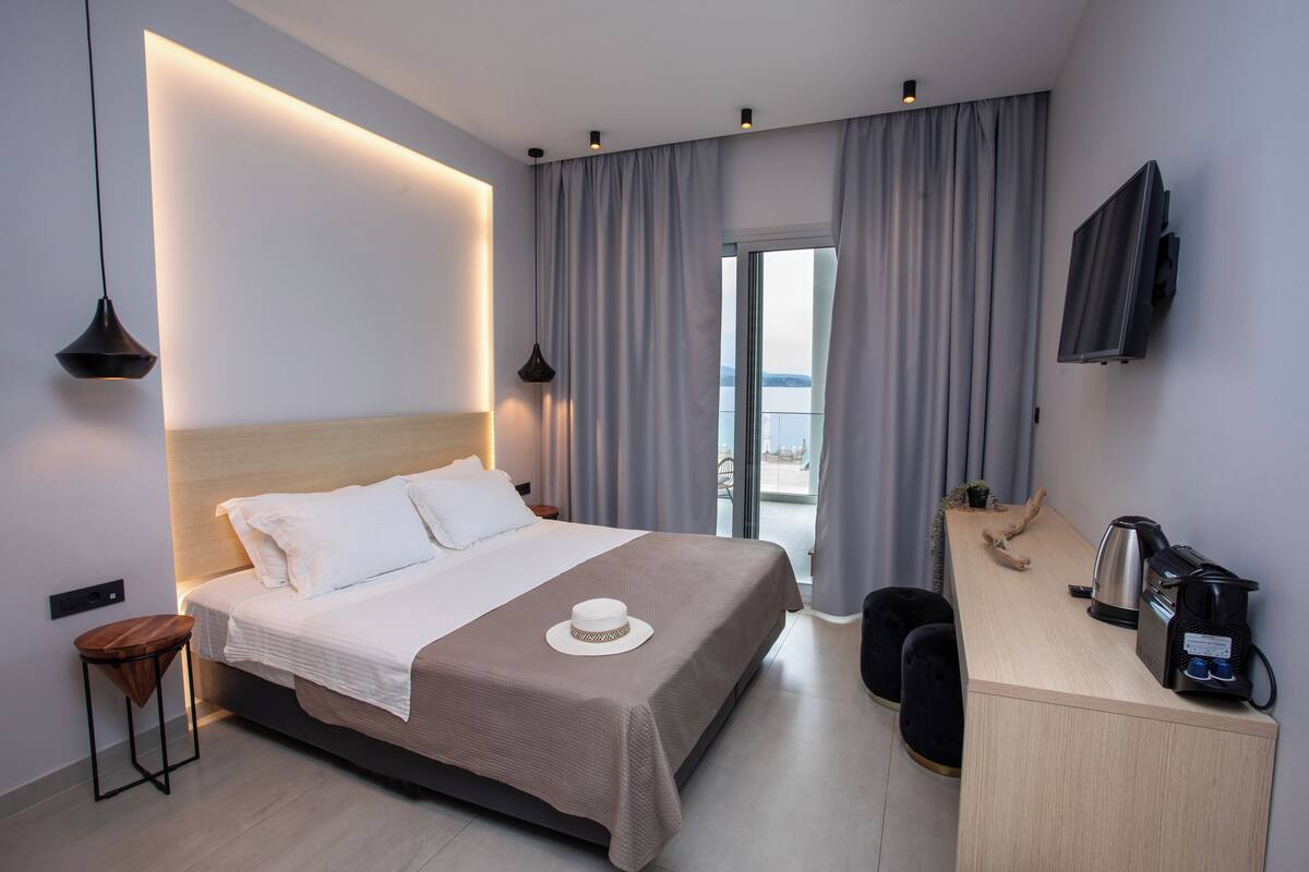 A modern hotel room with a large bed, a desk with a kettle, and a TV on the wall.