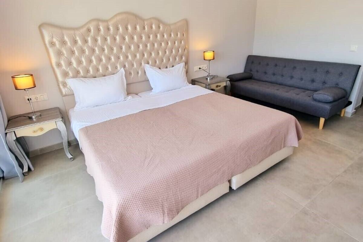 A bedroom with a large bed, a sofa, two bedside tables with lamps, and a ceiling light fixture.