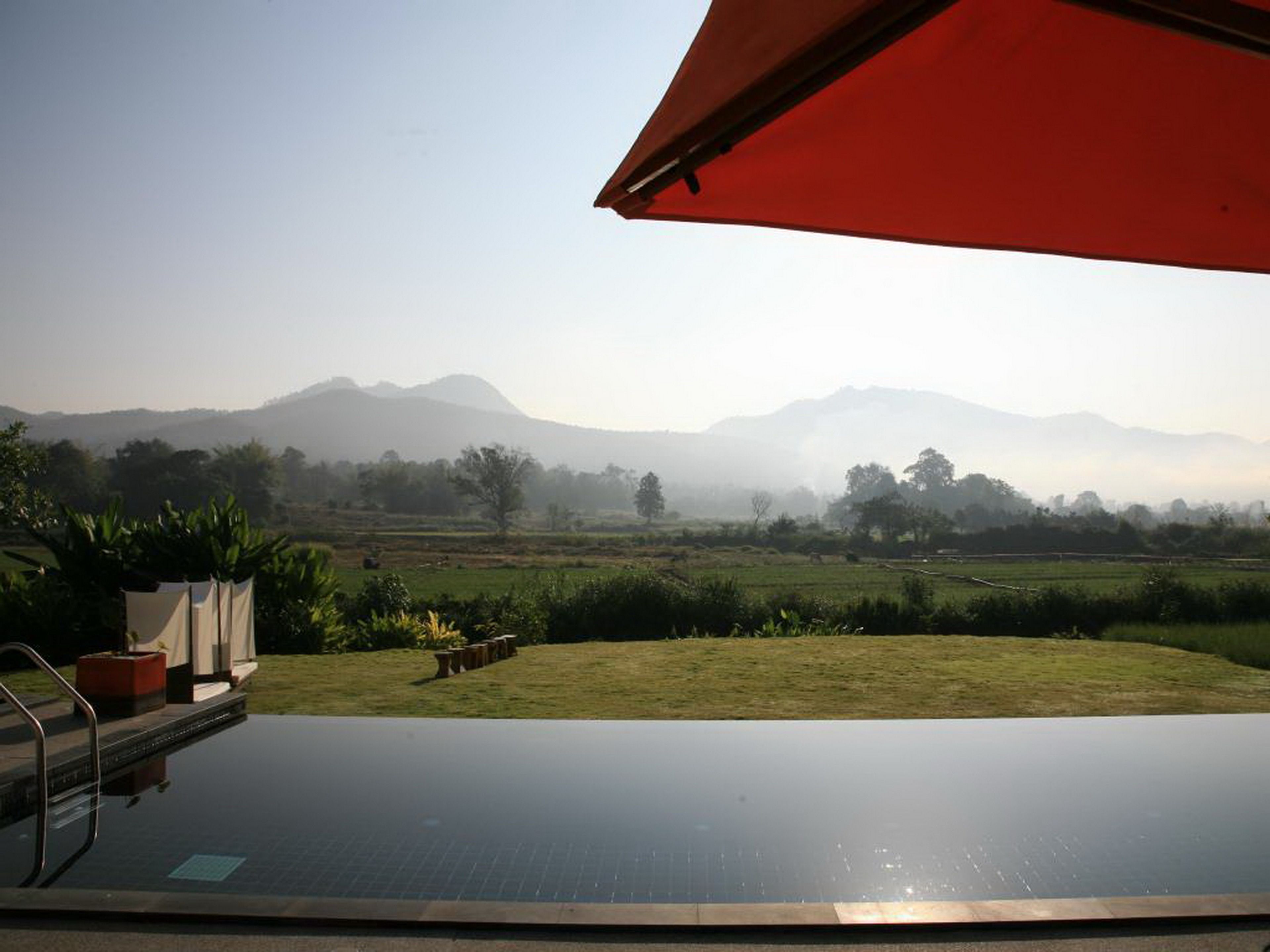 Ein Fernblick auf neblige Berge und eine grüne Landschaft über einem Infinity-Pool.
