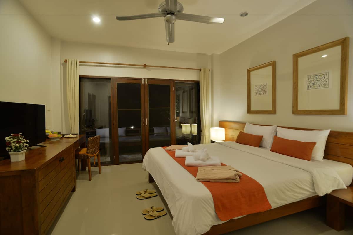 Quarto de hotel com cama, escrivaninha, cadeira, televisão e ventoinha no teto.