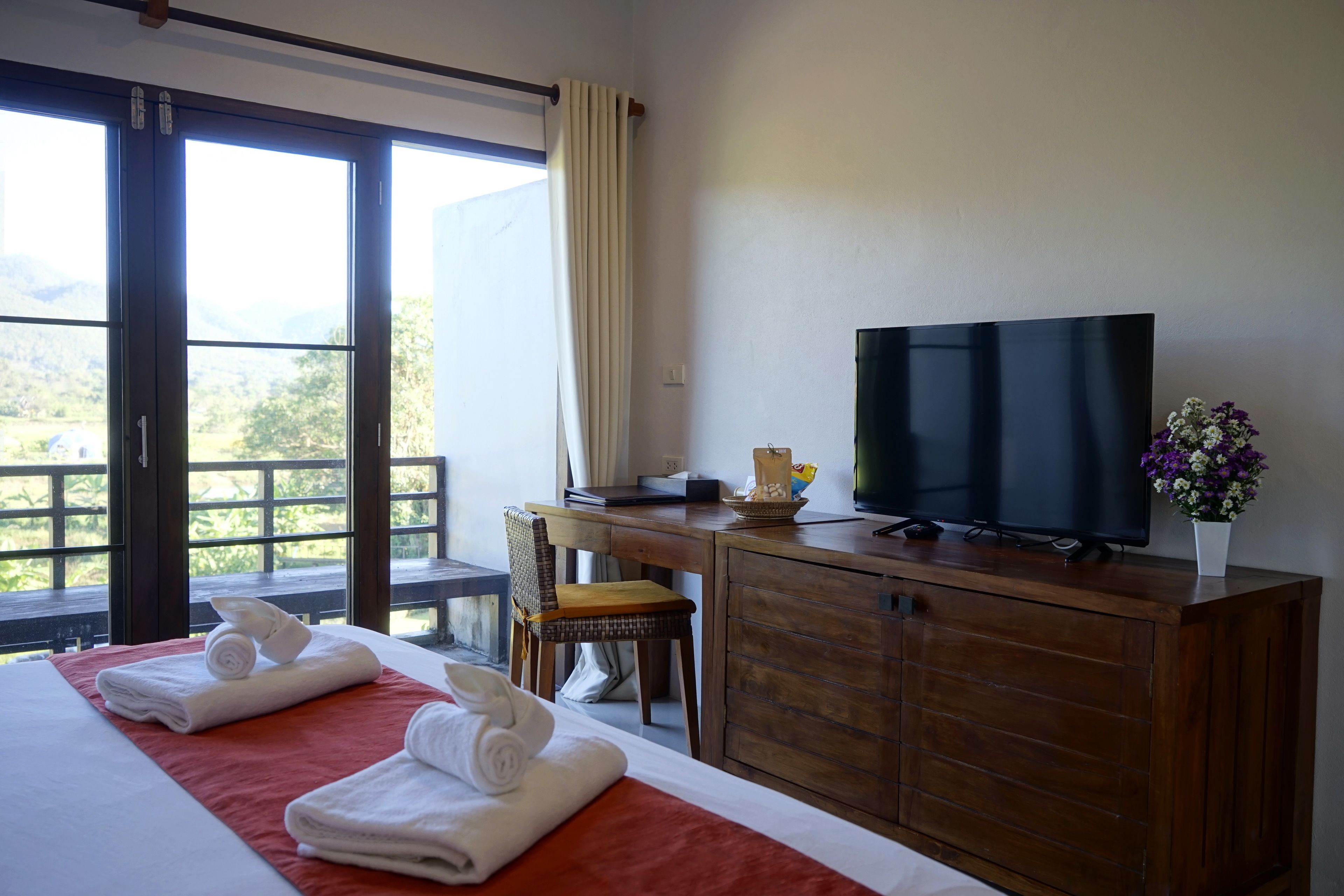 A hotel room with a bed, a desk with a television, a chair, and a view of the outdoors.