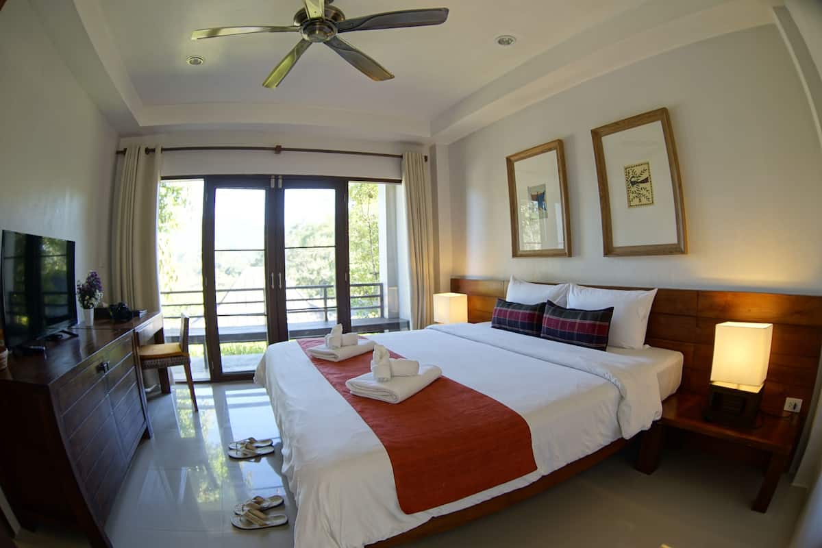 Quarto de hotel com uma cama grande, televisão, mesa de trabalho e varanda com cortinas.