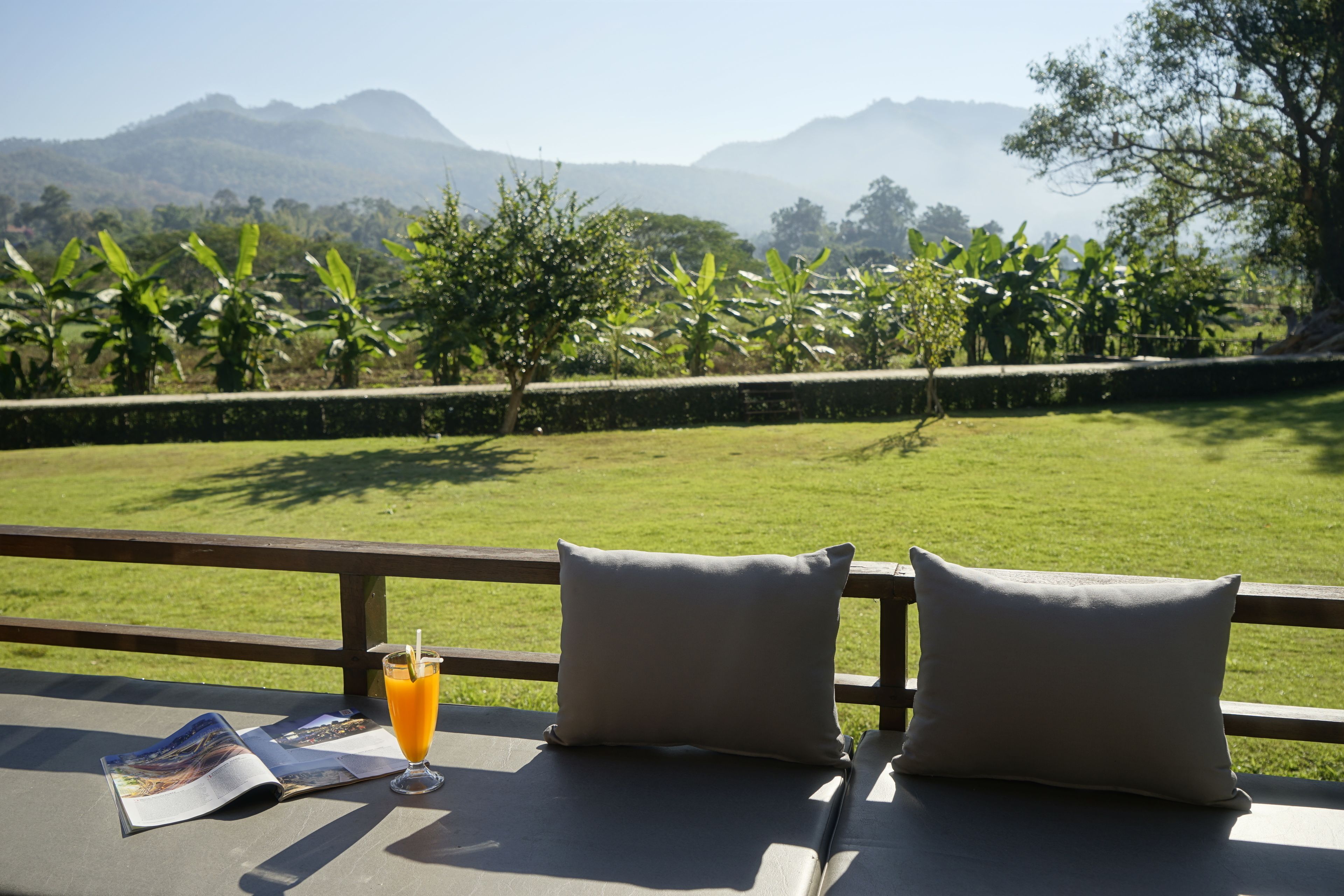 A view from a balcony with a table, two pillows, a glass of orange juice, and a magazine.