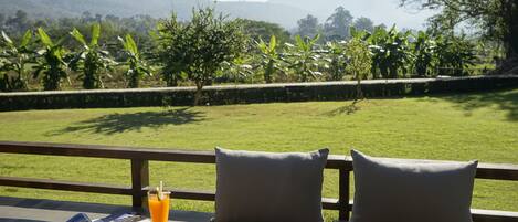 A view from a balcony with a table, two pillows, a glass of orange juice, and a magazine.