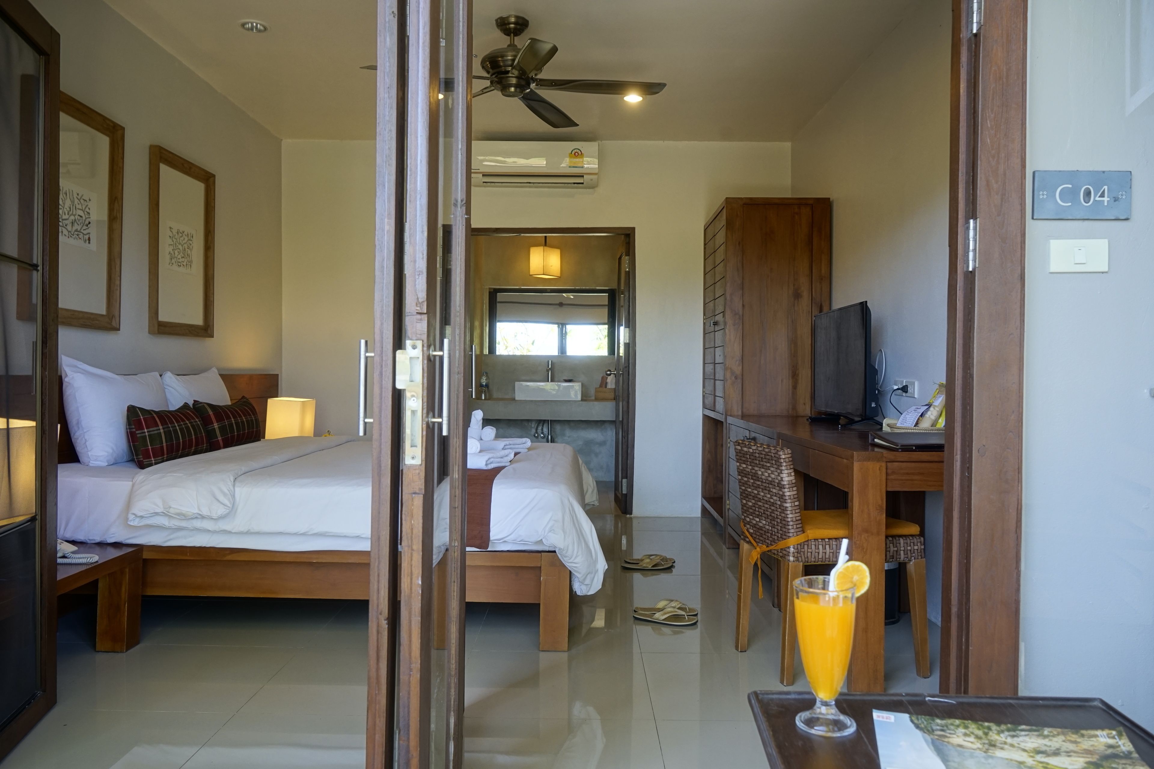 A hotel room with a bed, a desk with a computer, a TV, and a glass of orange juice on the table.