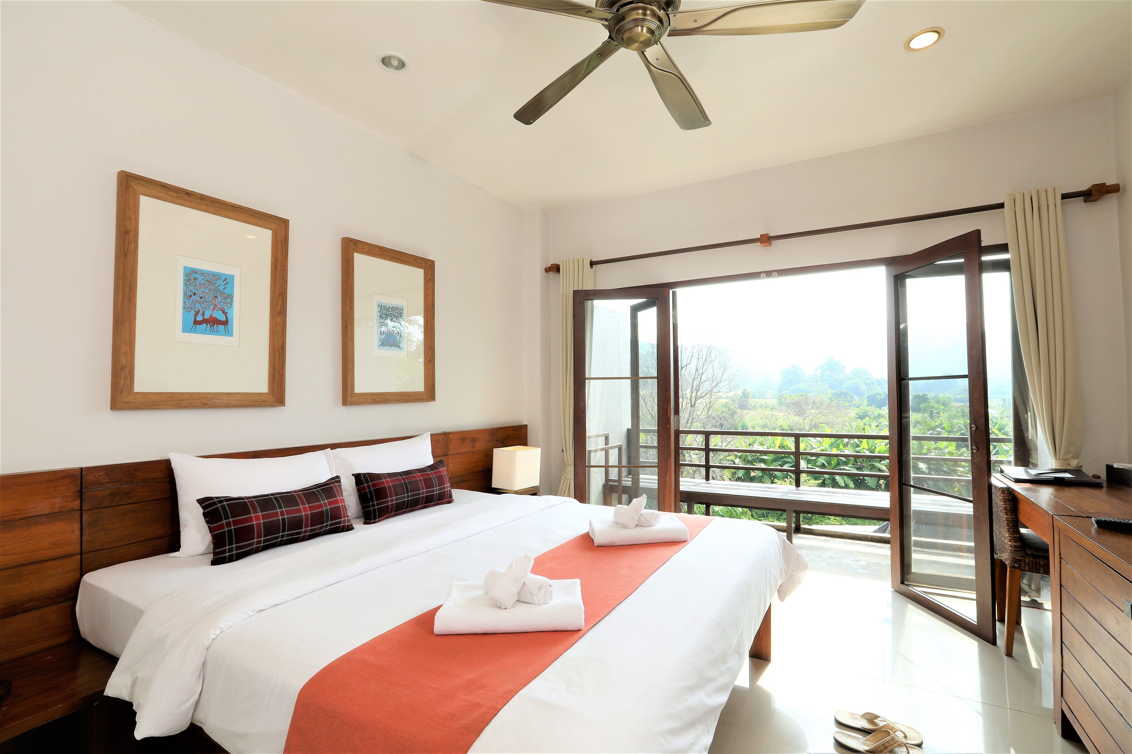 Ein Hotelzimmer mit Bett, Schreibtisch, Stuhl, Deckenventilator und einem Balkon mit Aussicht.