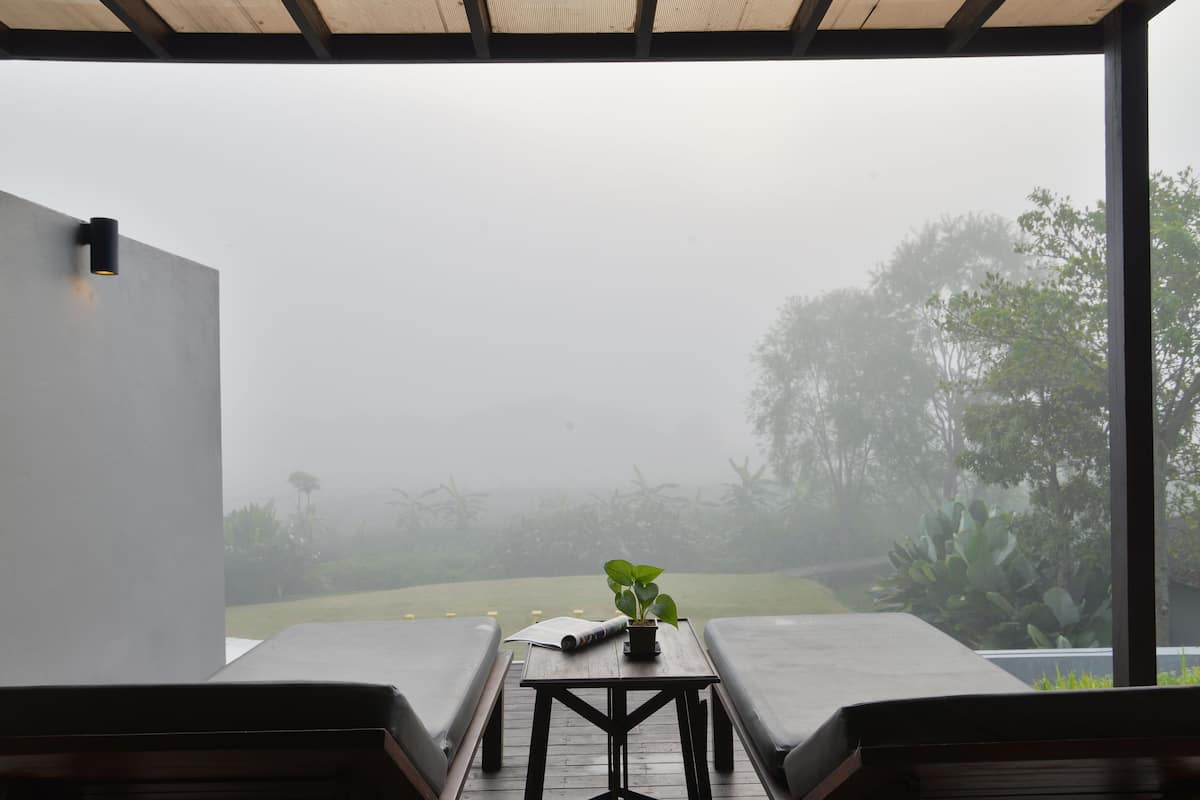 Uma área de estar moderna ao ar livre, com duas poltronas e uma mesa, com vista para um jardim.