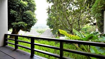 A balcony with a wooden railing overlooking a lush garden with various plants and trees.