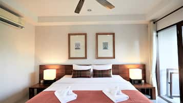 Une chambre d’hôtel avec un lit, deux tables de chevet avec des lampes, un ventilateur de plafond et des tableaux encadrés accrochés au mur.