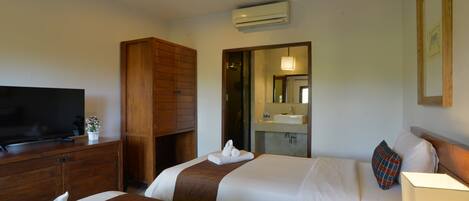 A hotel room with two beds, a TV, a wooden wardrobe, a ceiling fan, and a bathroom visible through an open door.