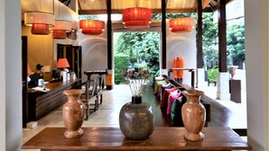 Un lobby espacioso con techo alto, ventanas amplias y una mesa de madera central con jarrones.