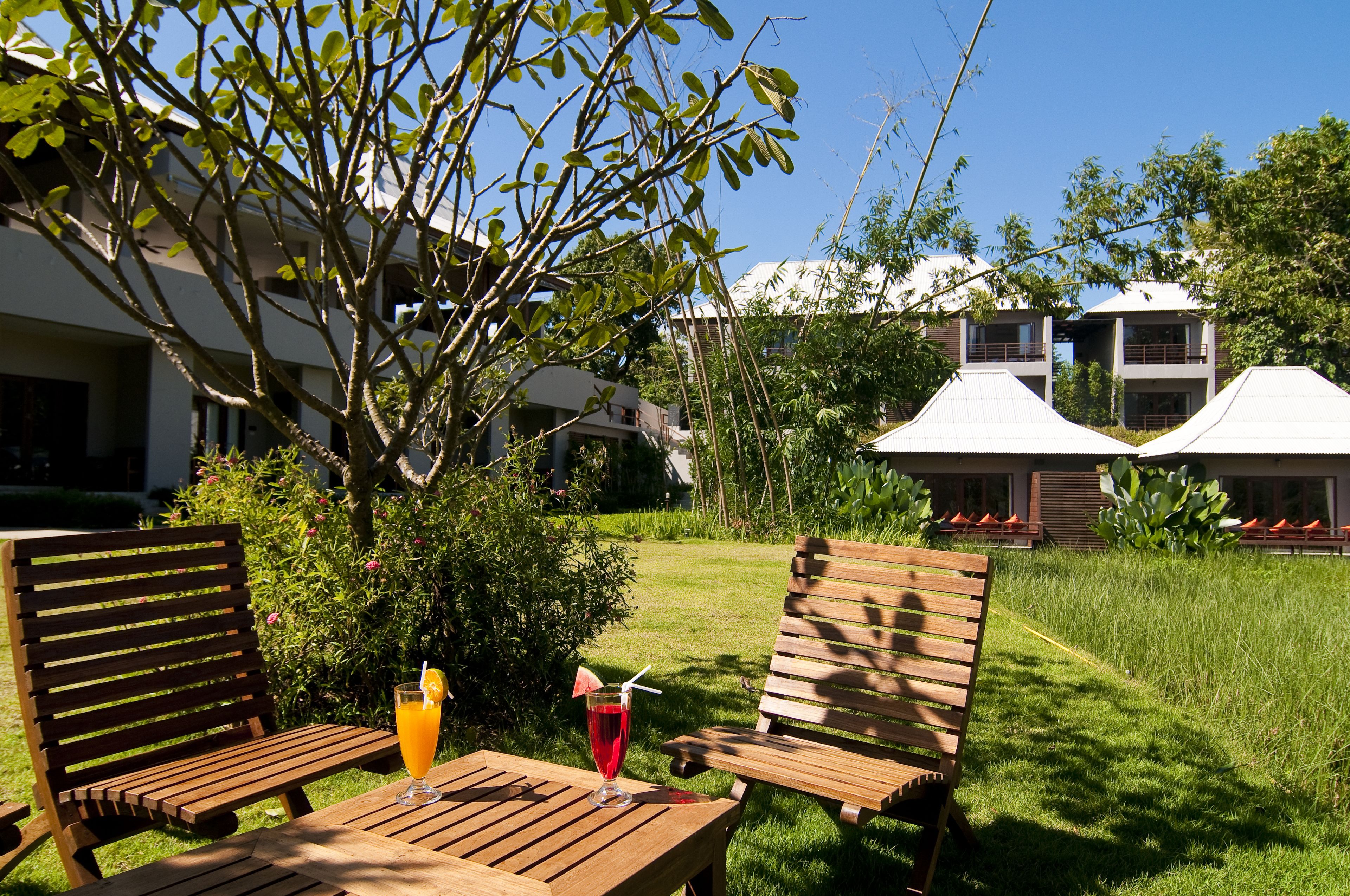A wooden table with two chairs and a glass of red drink with a straw and a lemon slice.