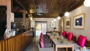 A reception area with a wooden reception desk, wicker seating, and a staircase leading to an upper level. - LILU PAI (Pai)