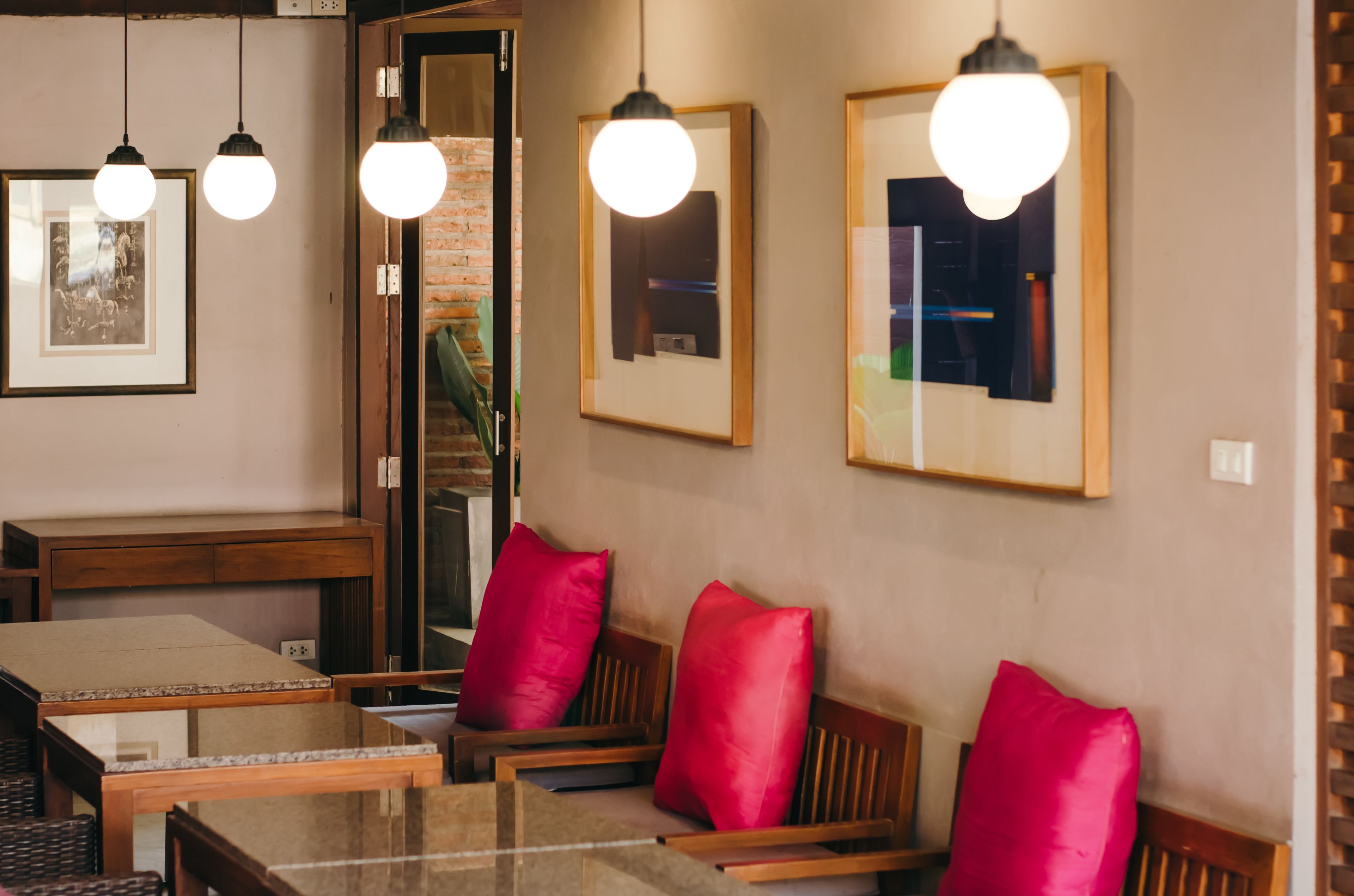 Uma sala de jantar com mesas e cadeiras de madeira, quadros nas paredes e luminárias pendentes.