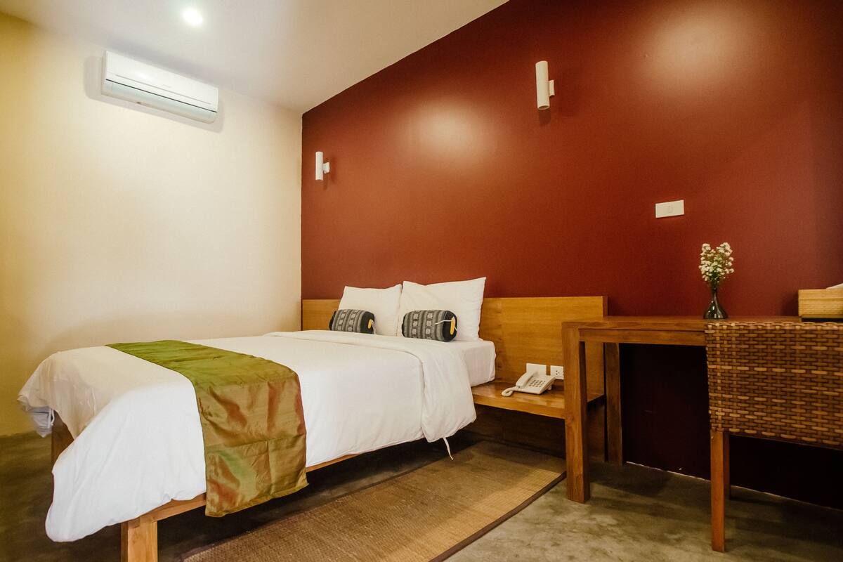 Una habitación de hotel con cama, mesita de noche y una pequeña mesa con un florero.