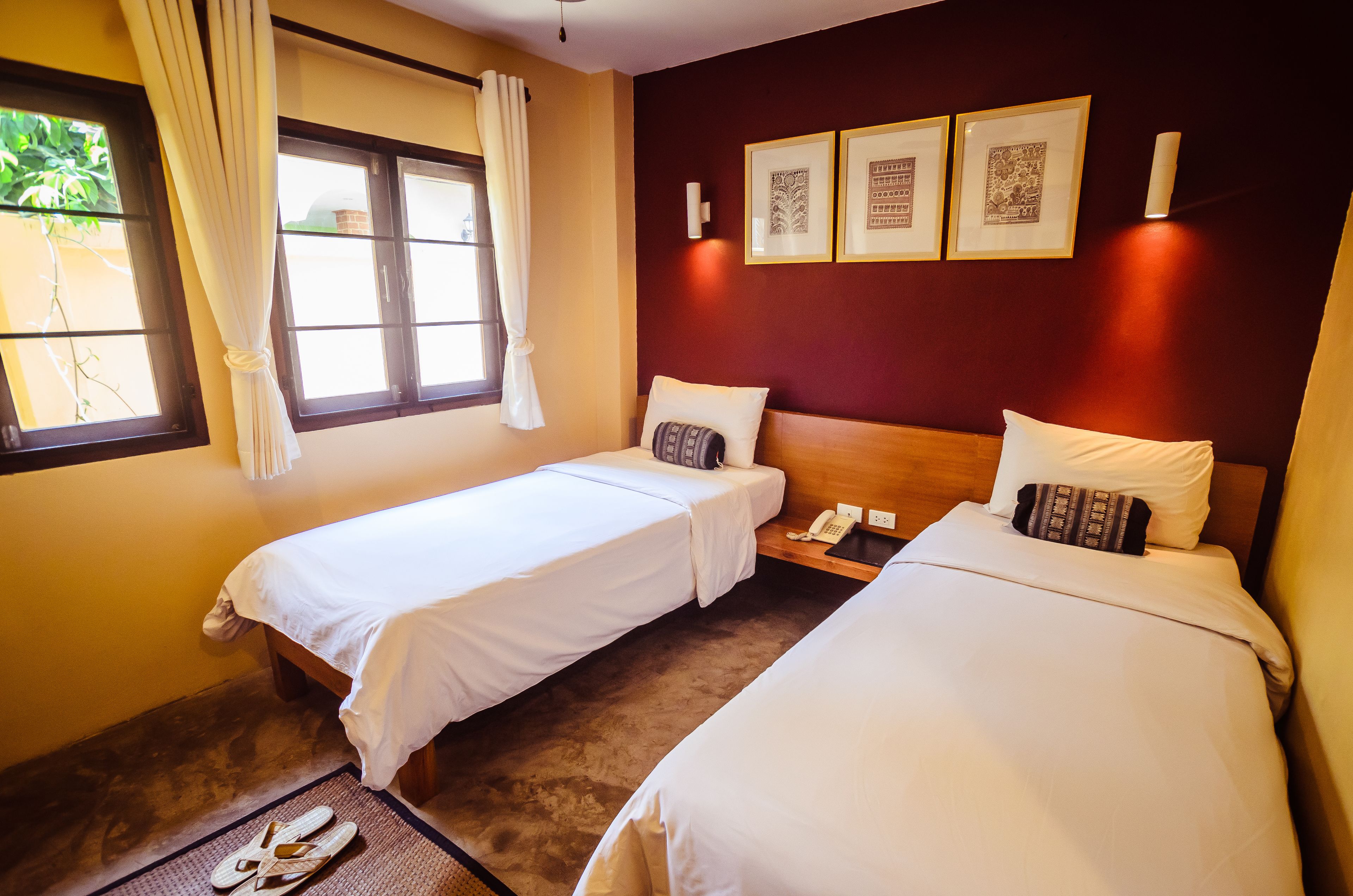 A hotel room with two single beds, a bedside table with a phone, and a window with curtains.
