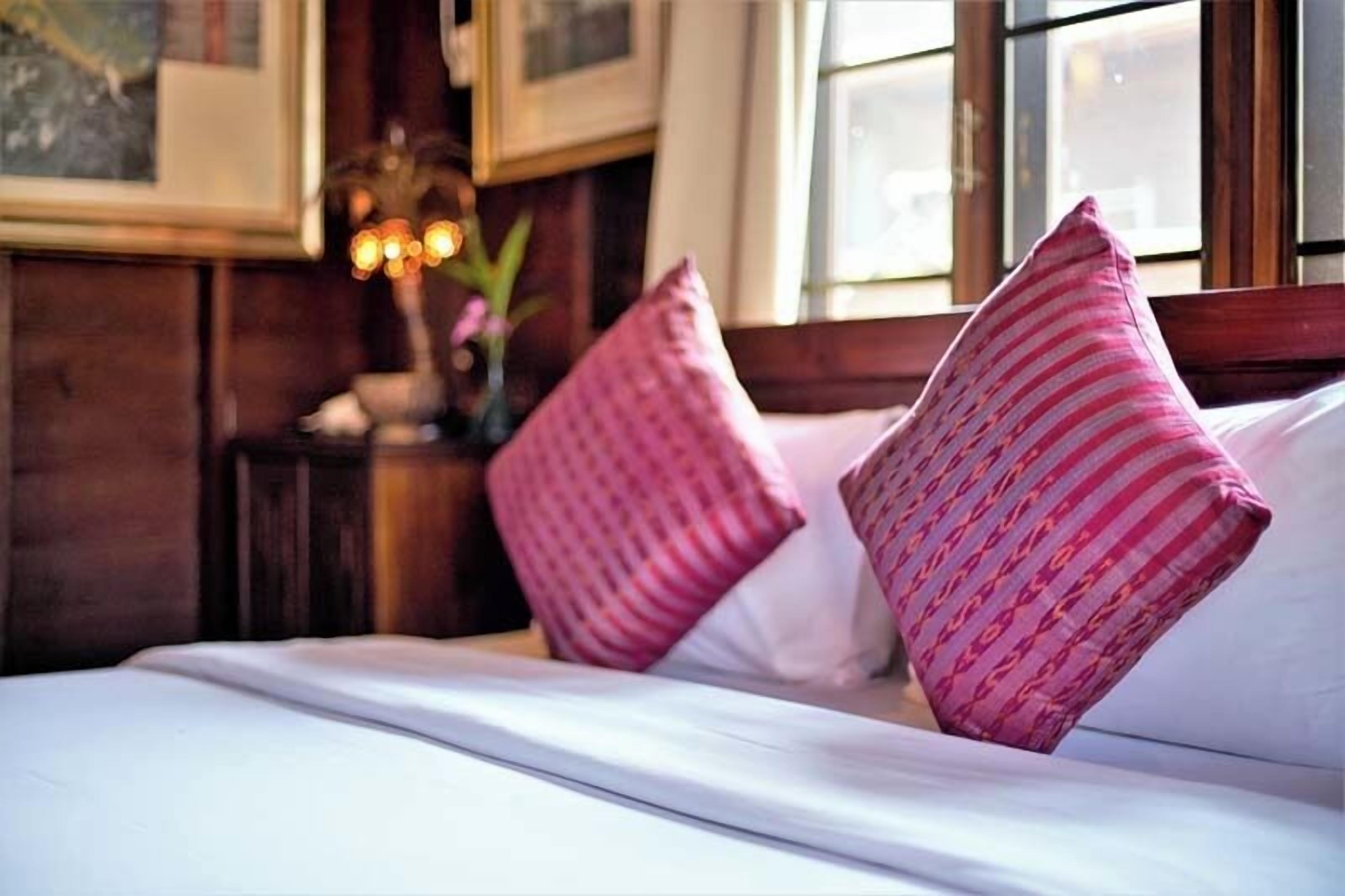 Una cama bien hecha con sábanas blancas y dos almohadas rosas con estampado.