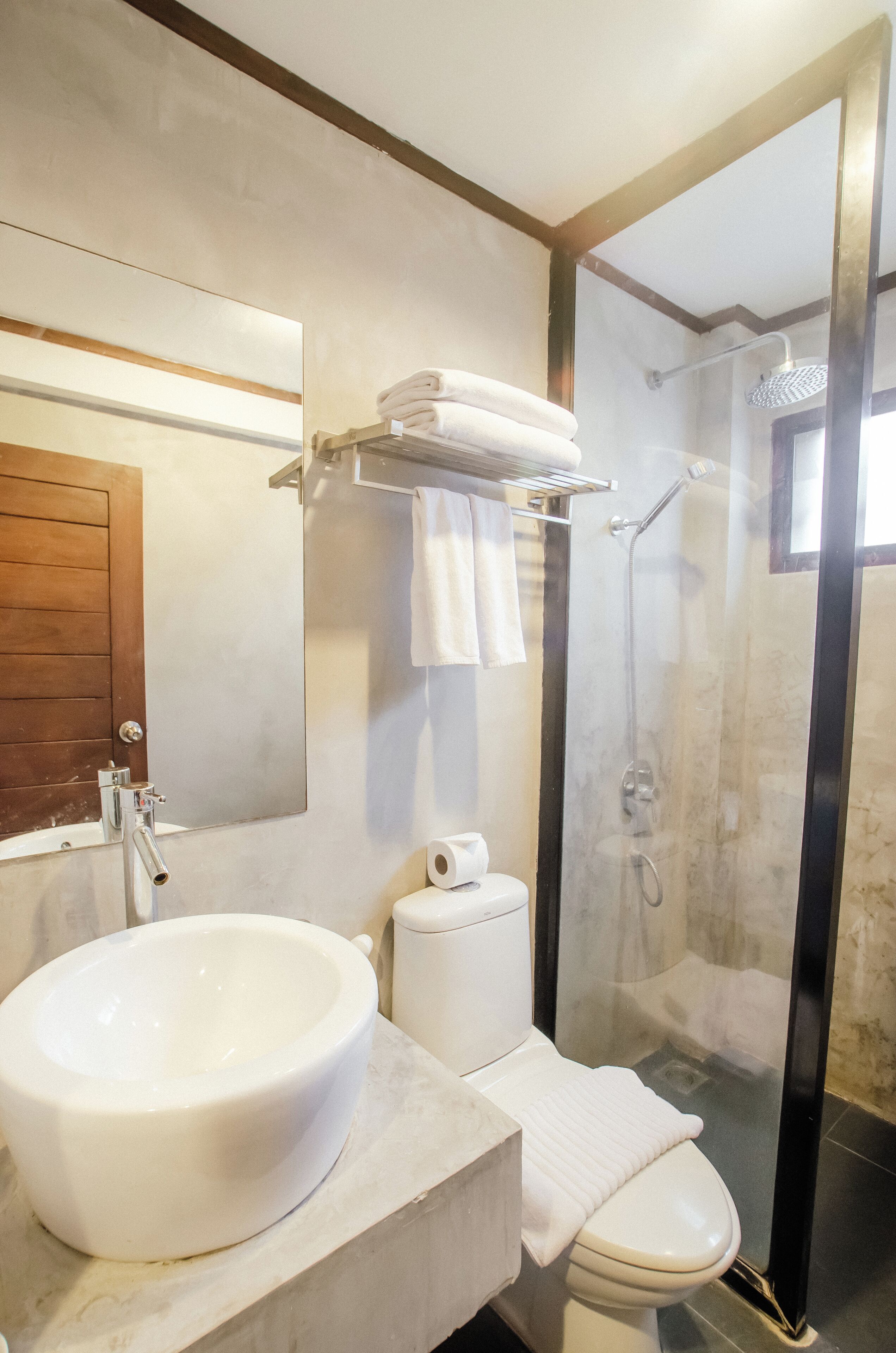 Un baño con un lavamanos grande de color blanco, un inodoro, ducha con mampara de vidrio y una puerta de madera.