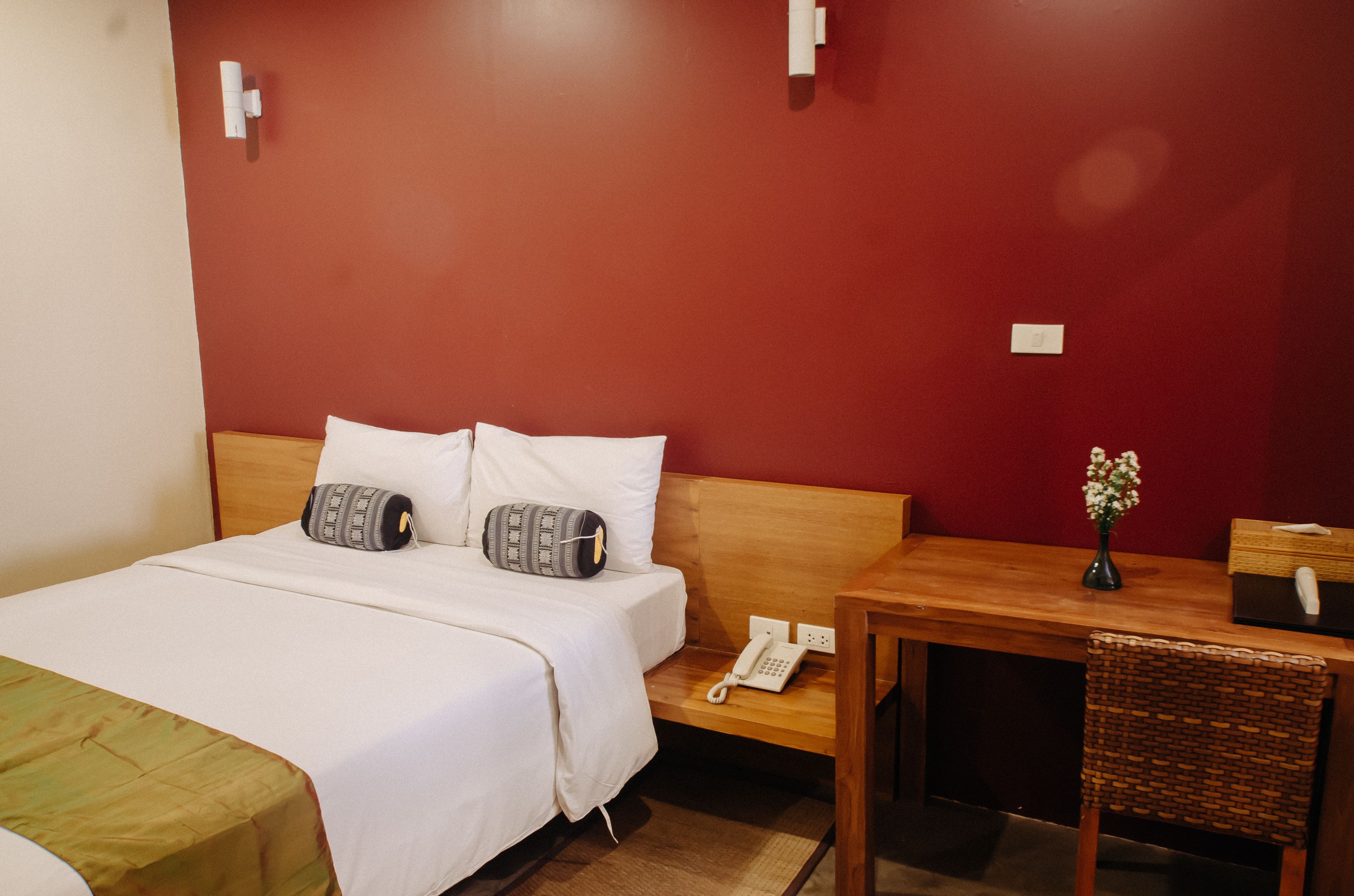 A hotel room with a bed, bedside table, and a small wooden table with a vase of flowers.