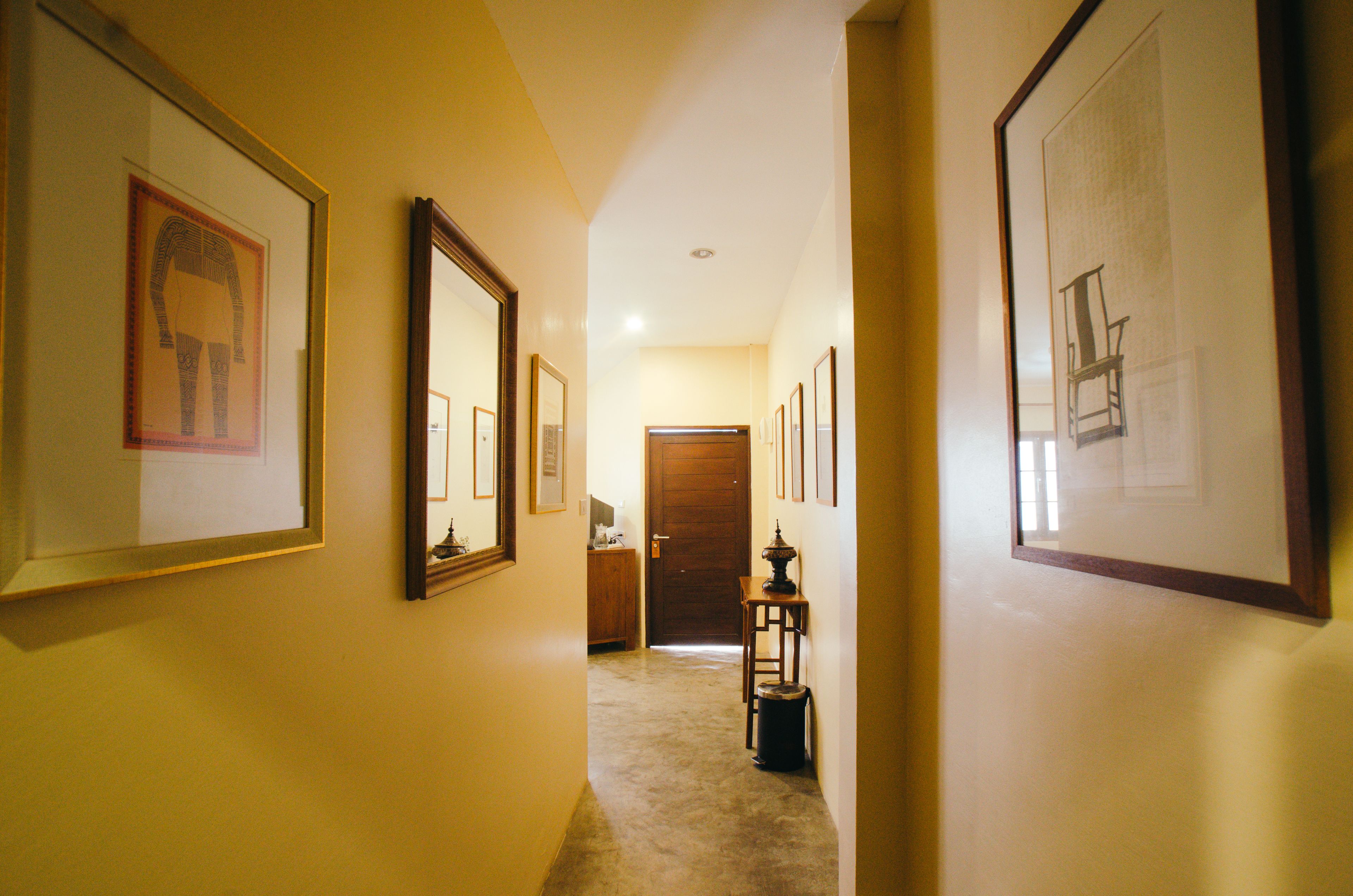 A hallway with framed artwork on the walls, a wooden door at the end, and a small table with a lamp.