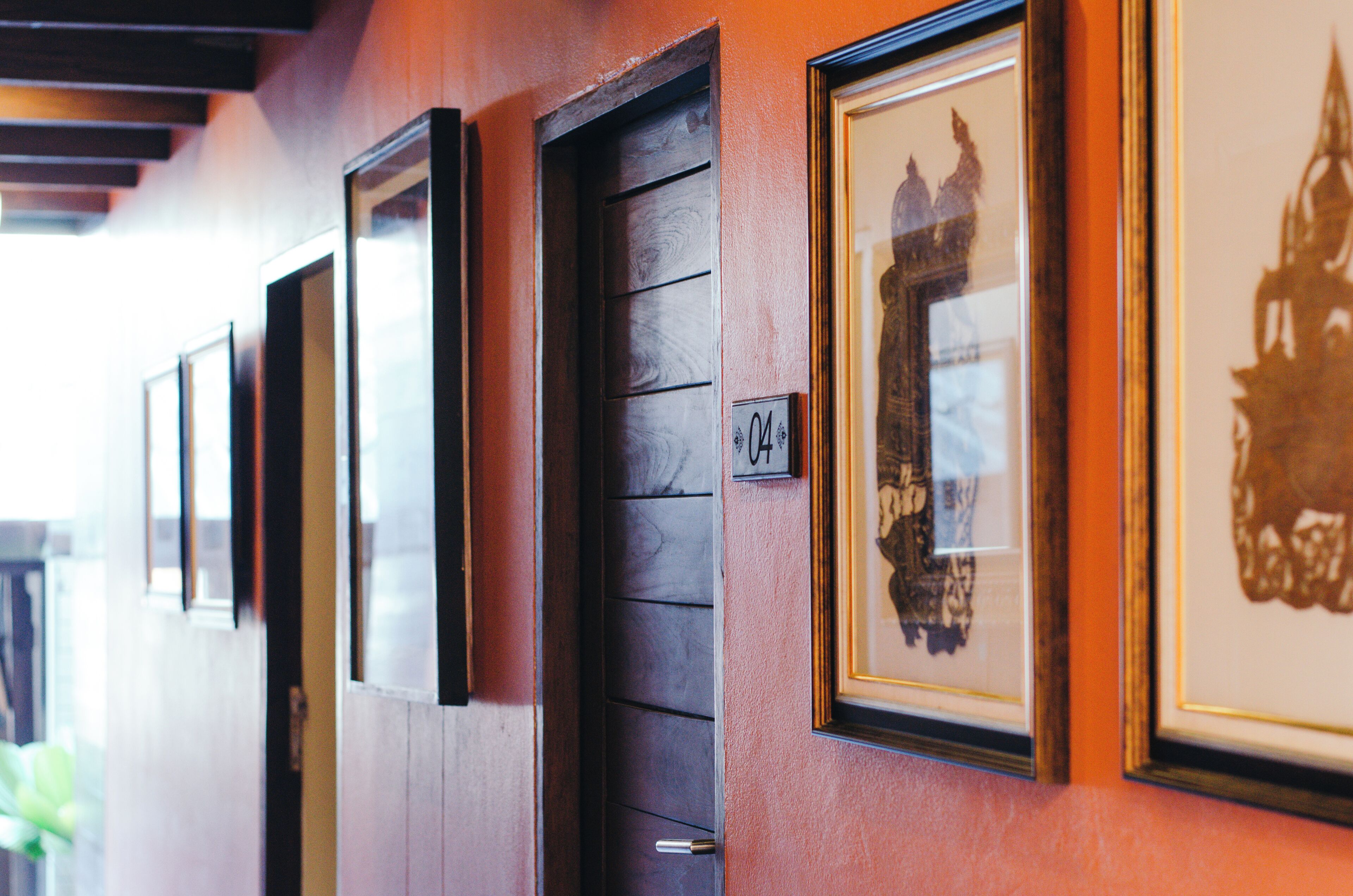 A hallway with framed artwork on the walls, wooden doors, and a visible room number.