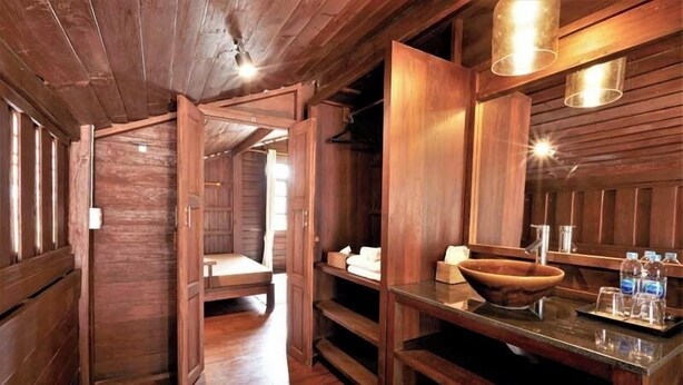 A wooden bathroom with a large wooden sink, a mirror, and a shelf with toiletries. - LILU PAI (Pai)