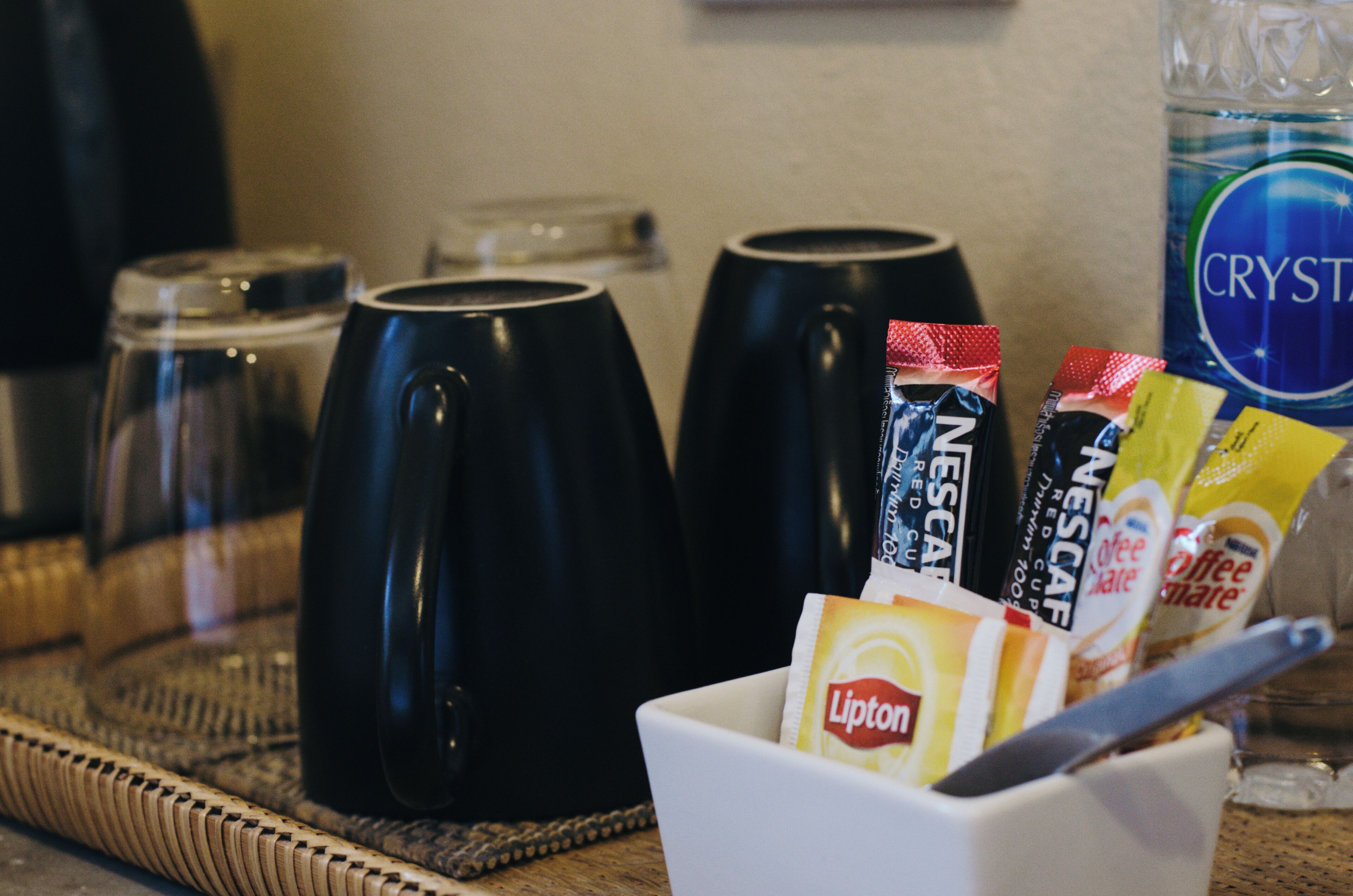 A coffee station with black cups, Lipton tea bags, and Nescafé instant coffee packets.