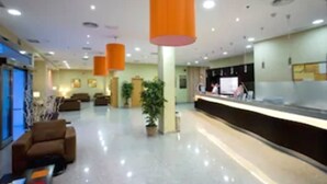 Un hall amplio con mostrador de recepción, asientos cómodos y plantas en macetas.