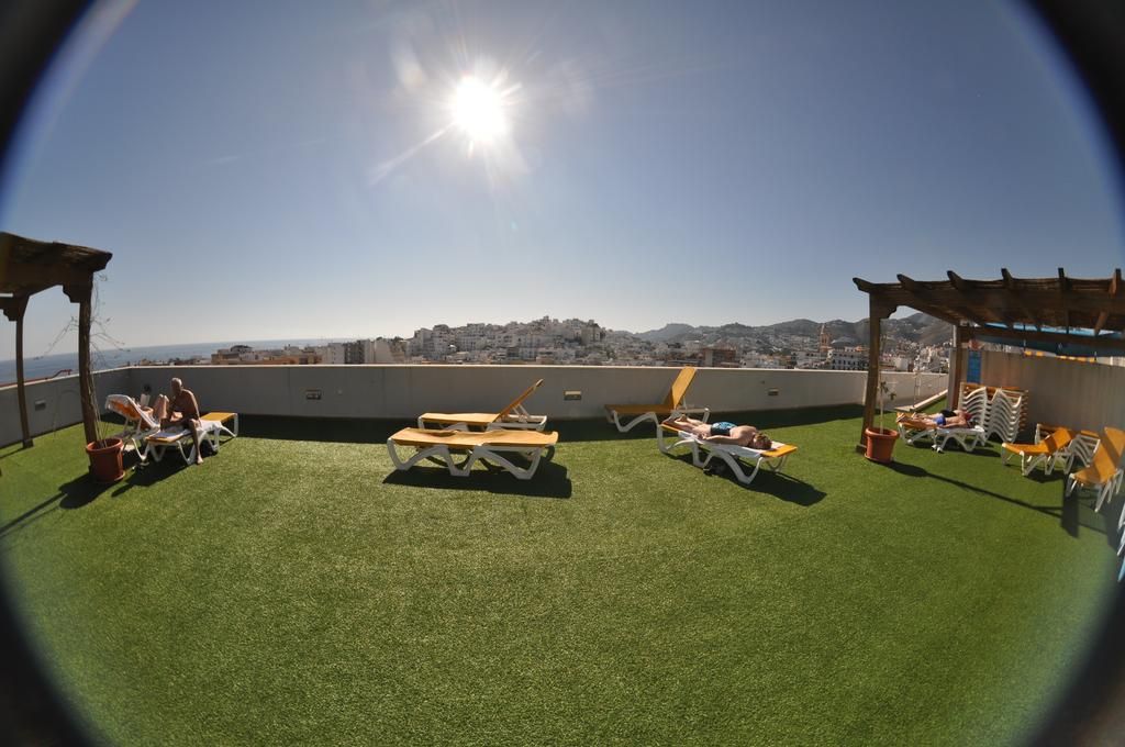 A rooftop terrace with artificial grass, sun loungers, and a wooden table.