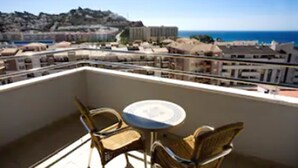 Un balcón con mesa y sillas, con vistas a un pueblo costero y al mar.