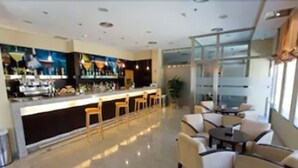 Un moderno vestíbulo de hotel con una zona de bar, arreglos de asientos y un amplio ventanal que proporciona luz natural.