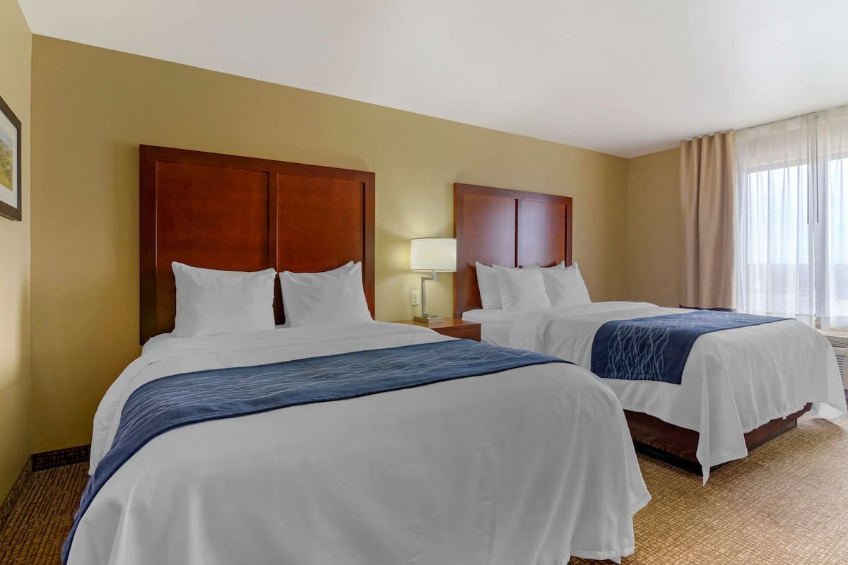 A hotel room with two beds, a nightstand with a lamp, and a window with curtains.
