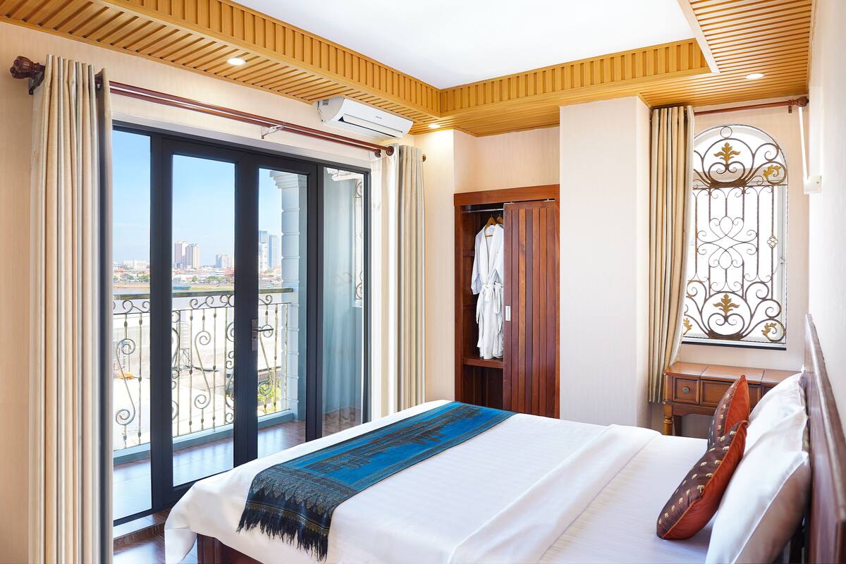 Habitación de hotel con una cama grande, un armario, una cómoda con espejo y un balcón con vistas a la ciudad.
