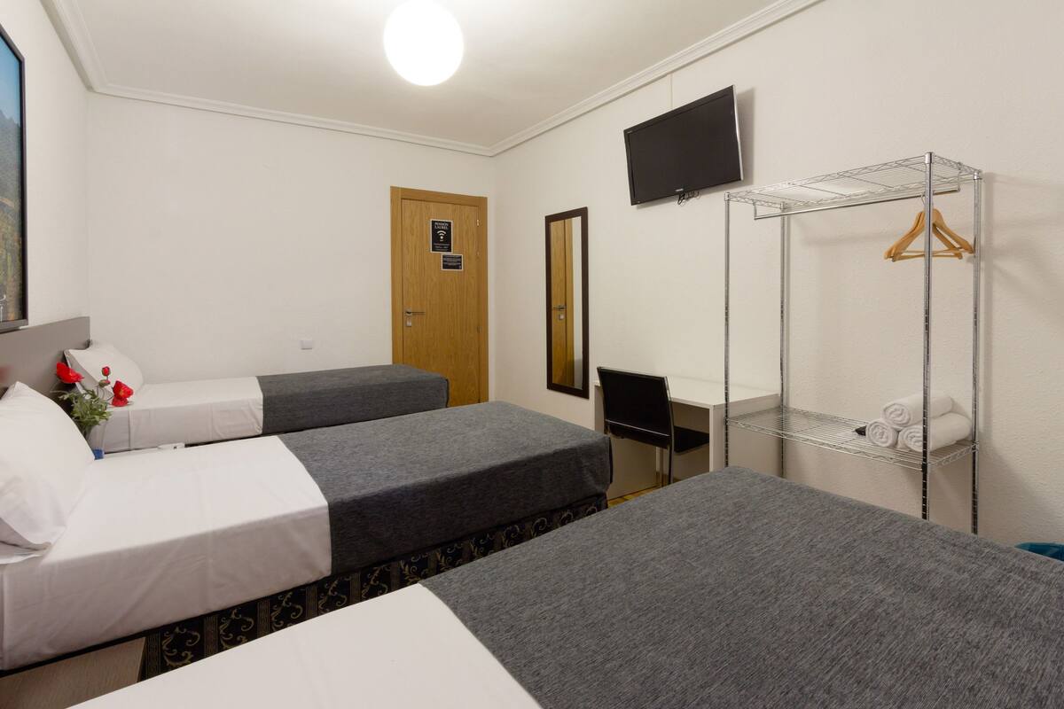 A hotel room with two beds, a desk, a TV, and a clothing rack.